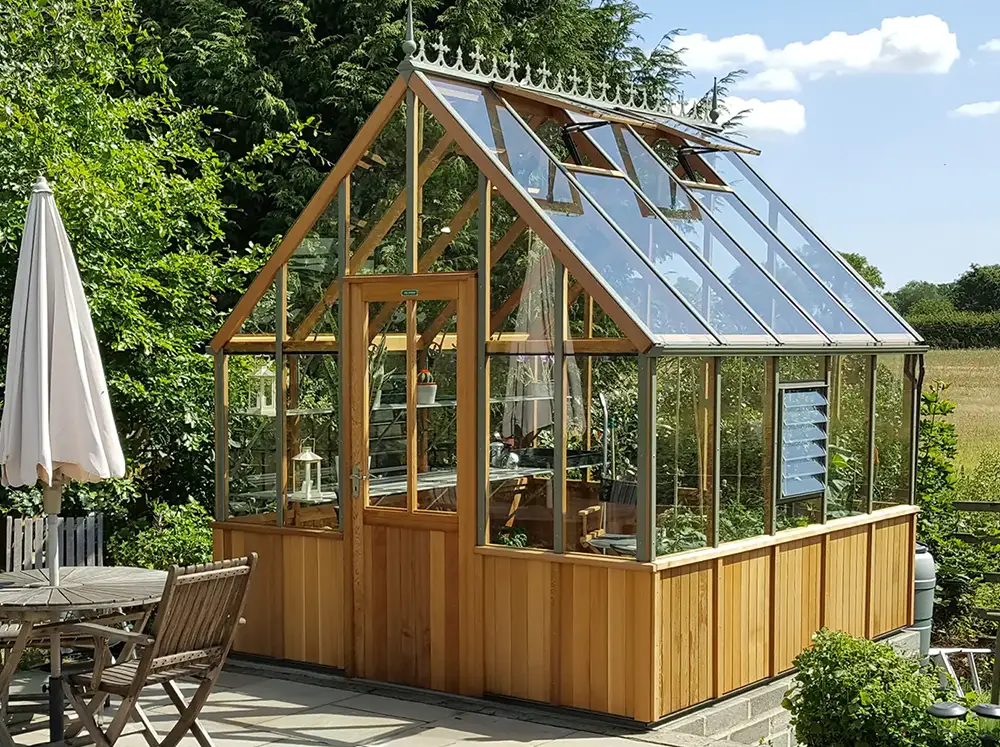 Beautiful sunny backyard with a Alton Cheltenham Greenhouse and some seating and umbrella to the side
