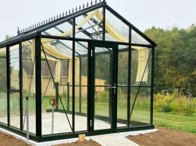 Gable end of a Janssens glass greenhouse with a Janssens Door Centering Kit installed with a single hinged door