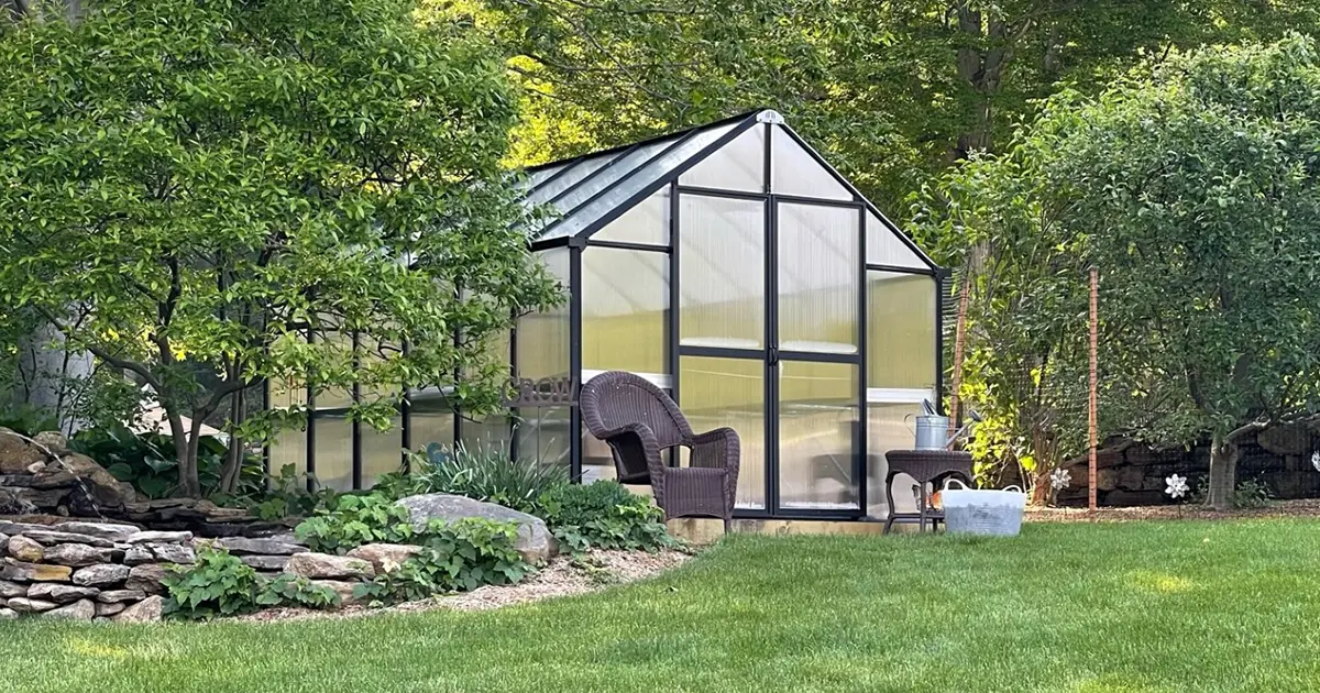 MONT greenhouse in a green backyard with a chair in front