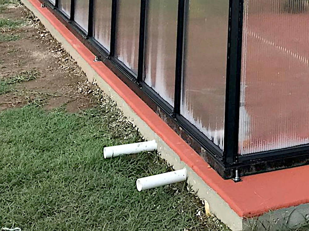 Close up of drainage pipes sticking out of a greenhouse foundation