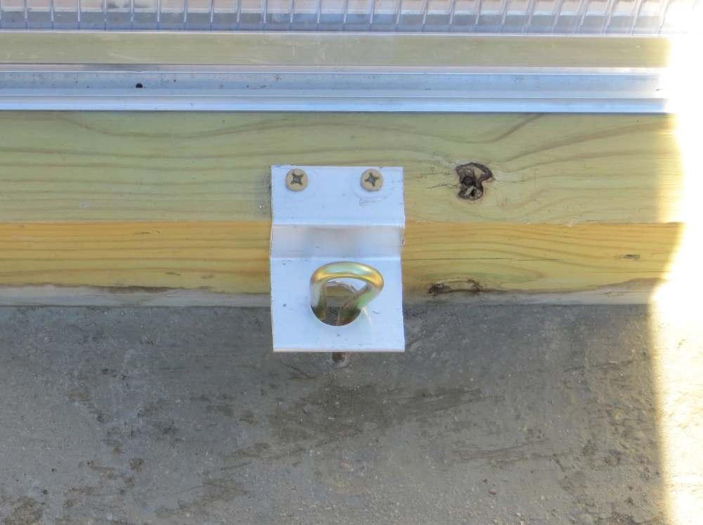 Close up of an anchor screwed into the foundation of a greenhouse