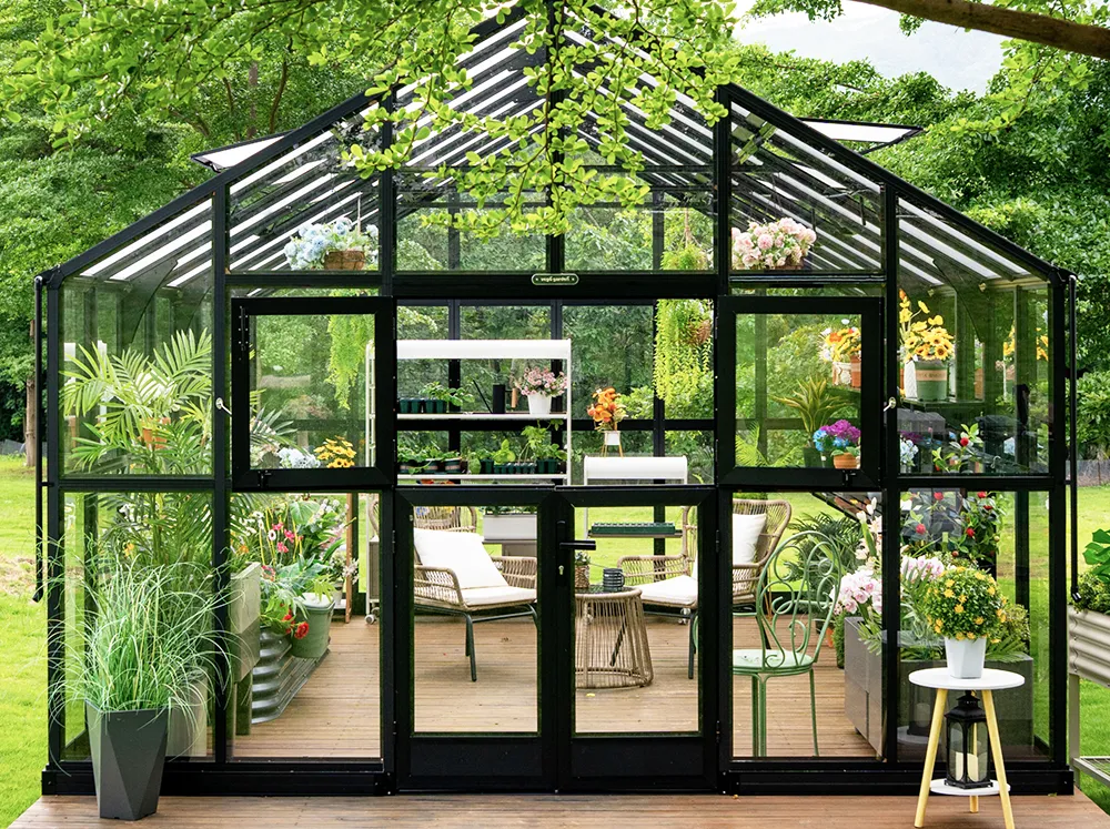 Front of the Vego Grand Victorian 12.5 Greenhouse with a seating area, raised bed and shelving inside