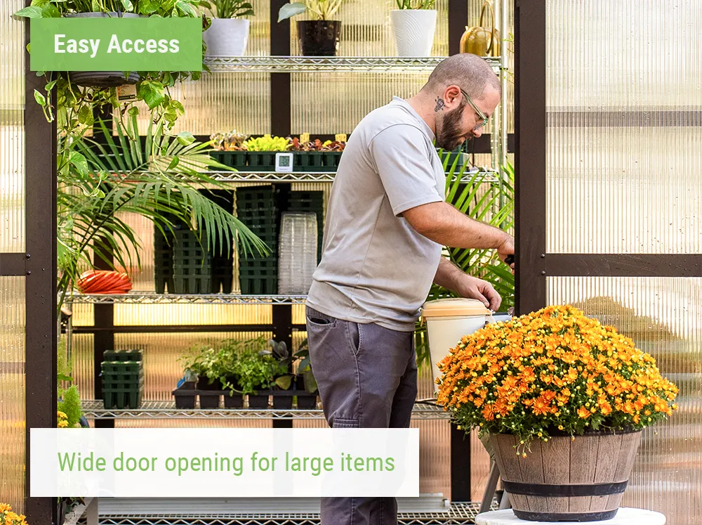 Wide door opening of the Vego Pacific 8.5 Greenhouse with a large planter in front and a person working inside the greenhouse