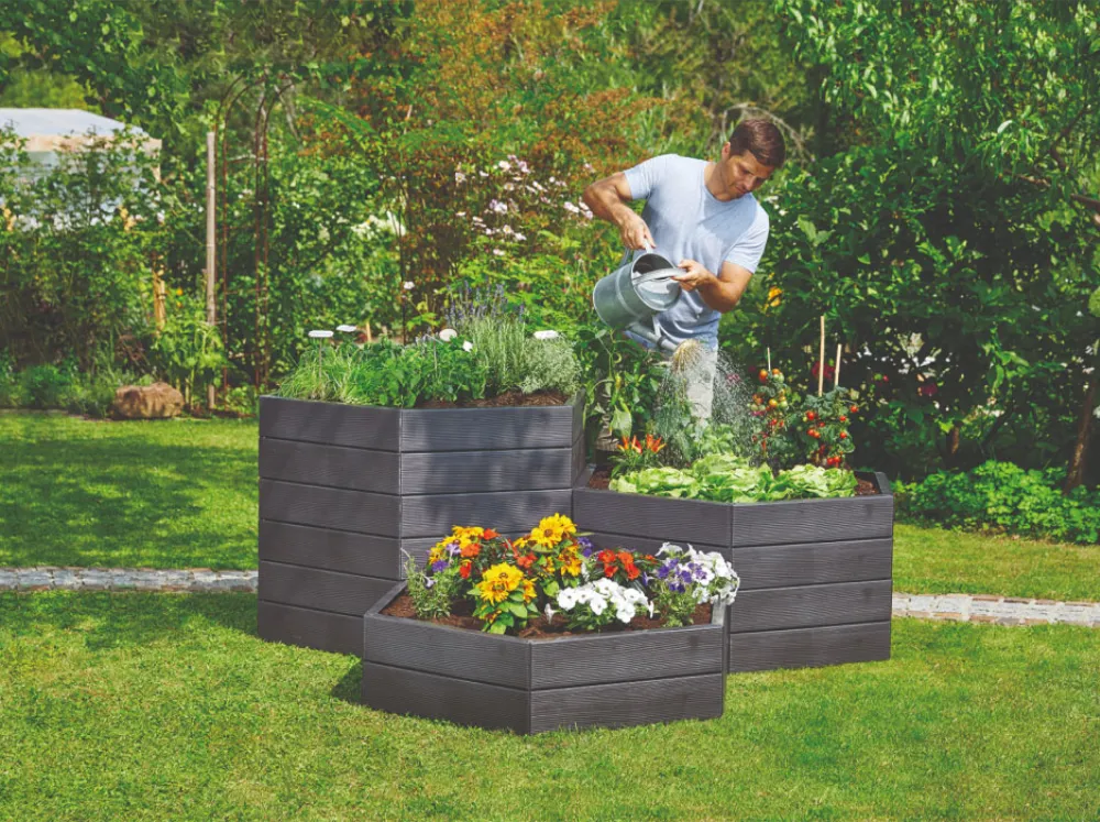 Different modular heights of Graf Hexagonal Raised Bed in backyard with person watering plants