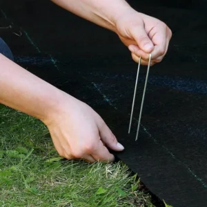 A person using a RSI Ground Covering Pin to fix RSI Ground Covering on a lawn