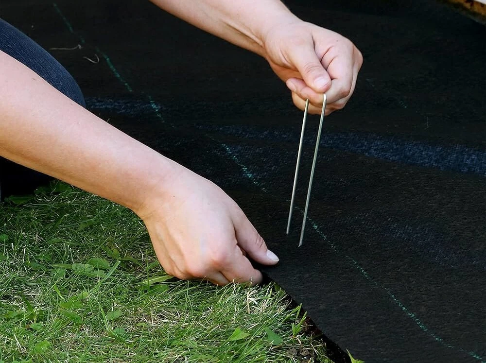 A person using a RSI Ground Covering Pin to fix RSI Ground Covering on a lawn